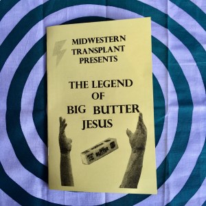 Midwestern Transplant Presents: The Legend of Big Butter Jesus by L.M. Zoller. Photo of a booklet zine printed on yellow paper. There are black and white cutouts of a long stick of butter, the arms of the King of Kings status, and a lightening bolt.
