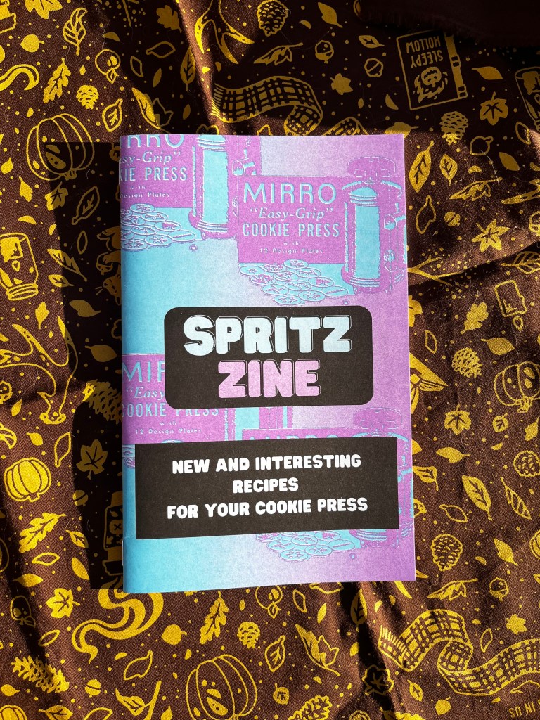 Cover image of Spritz Zine: New and Interesting Recipes for Your Cookie Press. Photo of cover, which has a repeating image of a vintage Mirro "easy grip" cookie press ad in blue and purple.